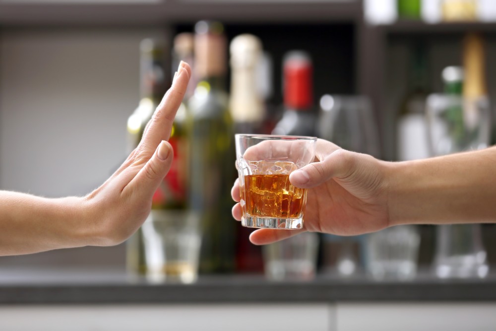A hand rejecting a glass of alcohol that is being handed to them